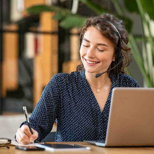 Picture of woman with headset on next to laptop