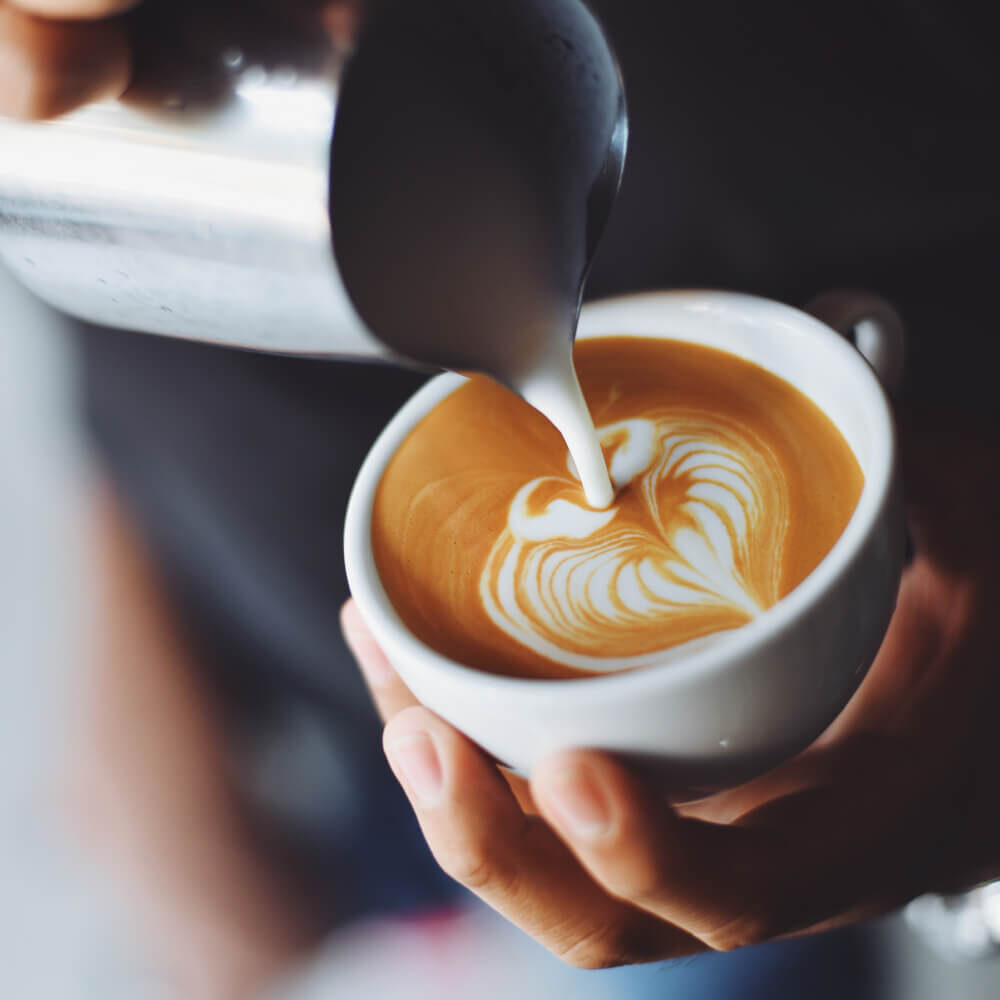 Picture of barista pouring milk into a coffee from milk jug