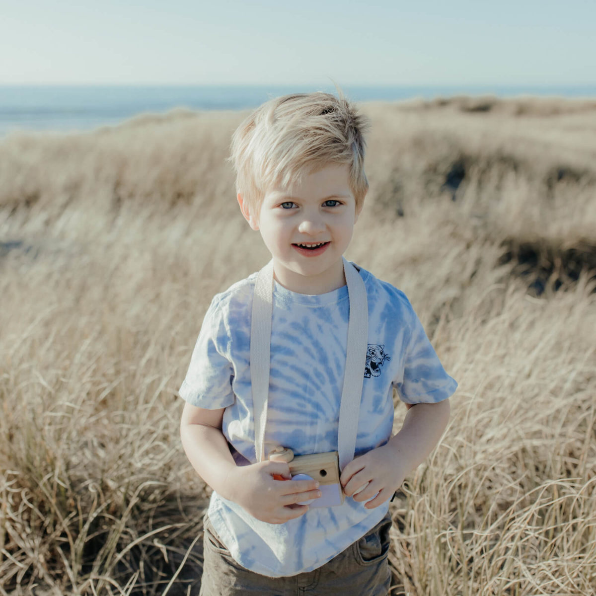 Picture of young boy in sand dunes at beach holding toy camera
