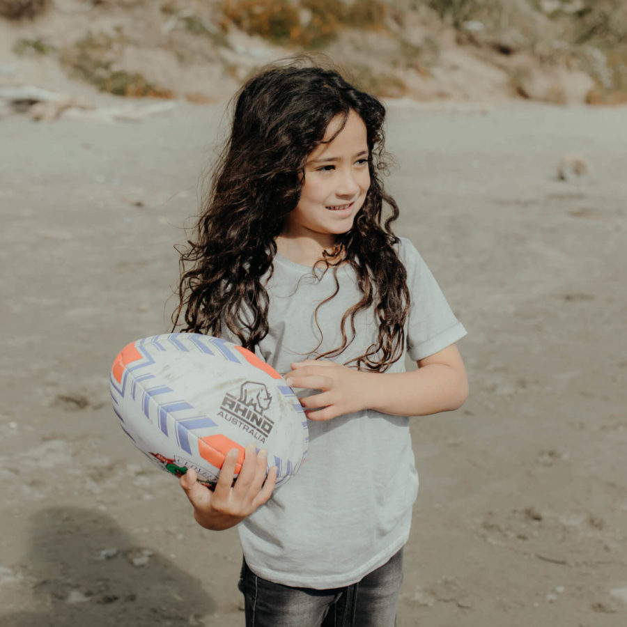 Picture of young girl on beach holding a rugby ball