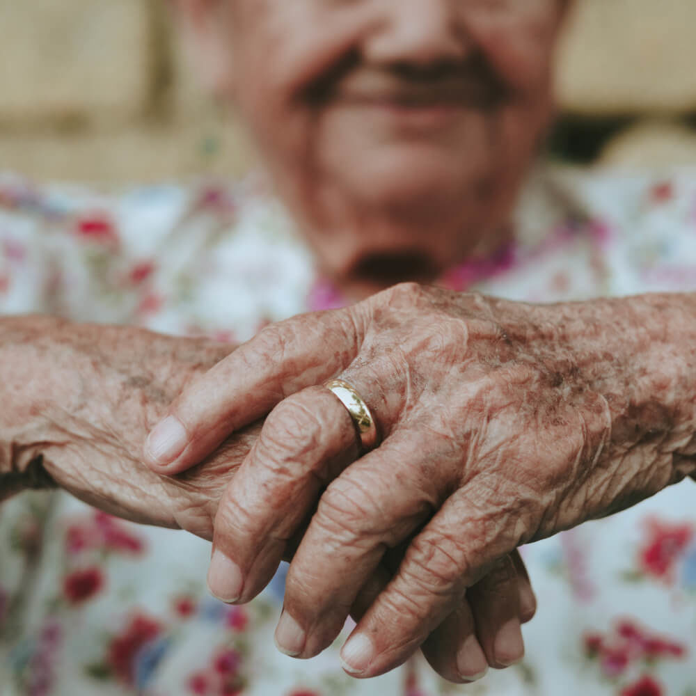 Picture of elderly mans hands with him smiling in background